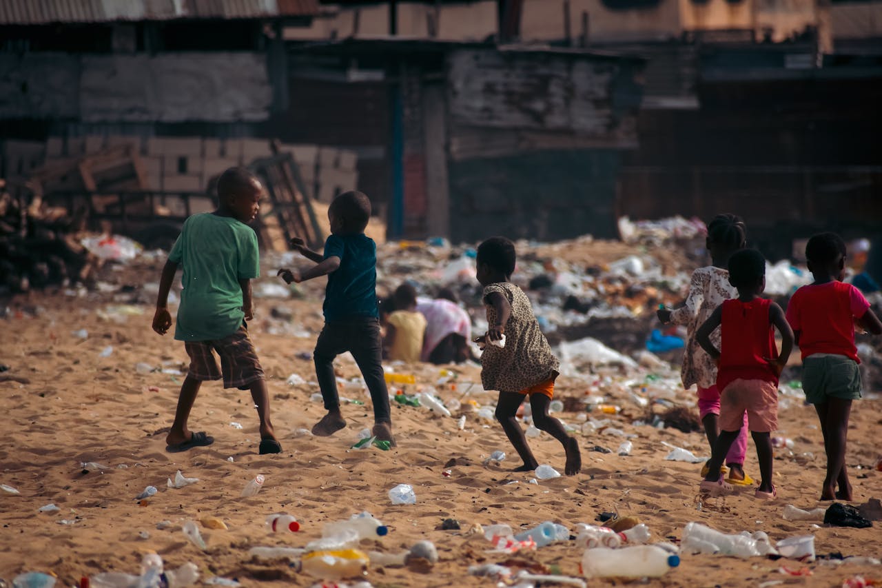 hero-img-01 Children play on a waste-covered urban beach, highlighting pollution and climate challenges.